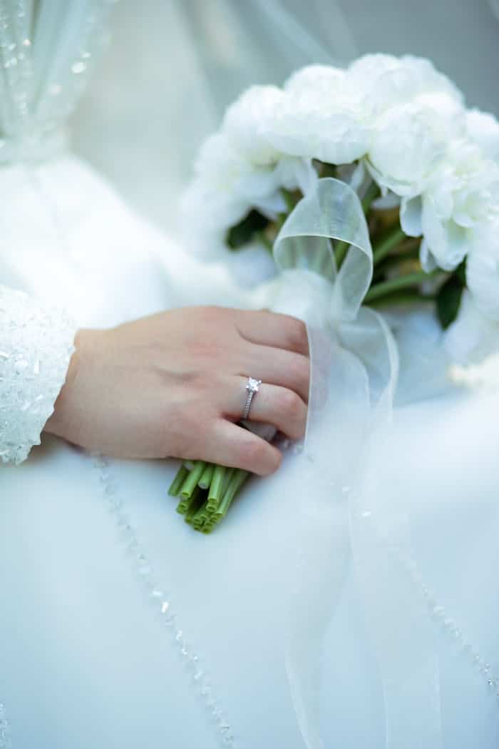 services-04 A bride's hand holding a white floral bouquet, showcasing an elegant wedding ring.